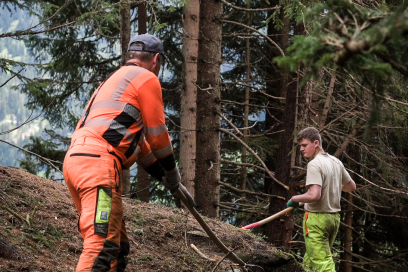 Arbeitseinsatz bei Holzräumungen gemeinsam mit dem Forst. Ein Förster und ein junger Mann rechen einen Waldboden,