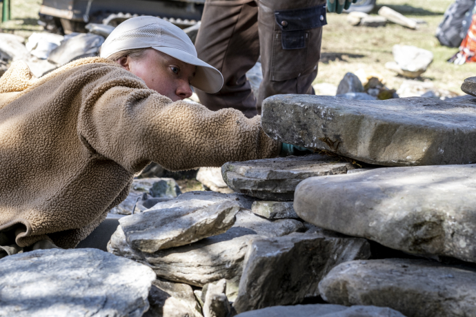 Bau an Strockensteinmauer Splügen. Eine Frau setzt Steine in eine Trockensteinmauer.